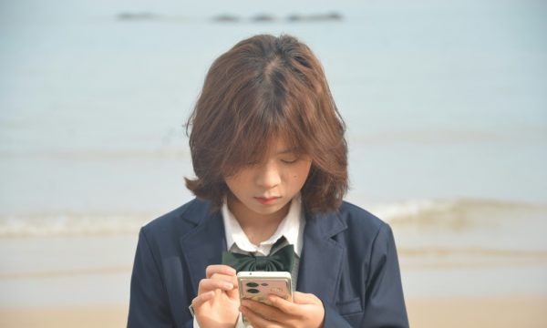 Girl in uniform looks at her phone by the sea.